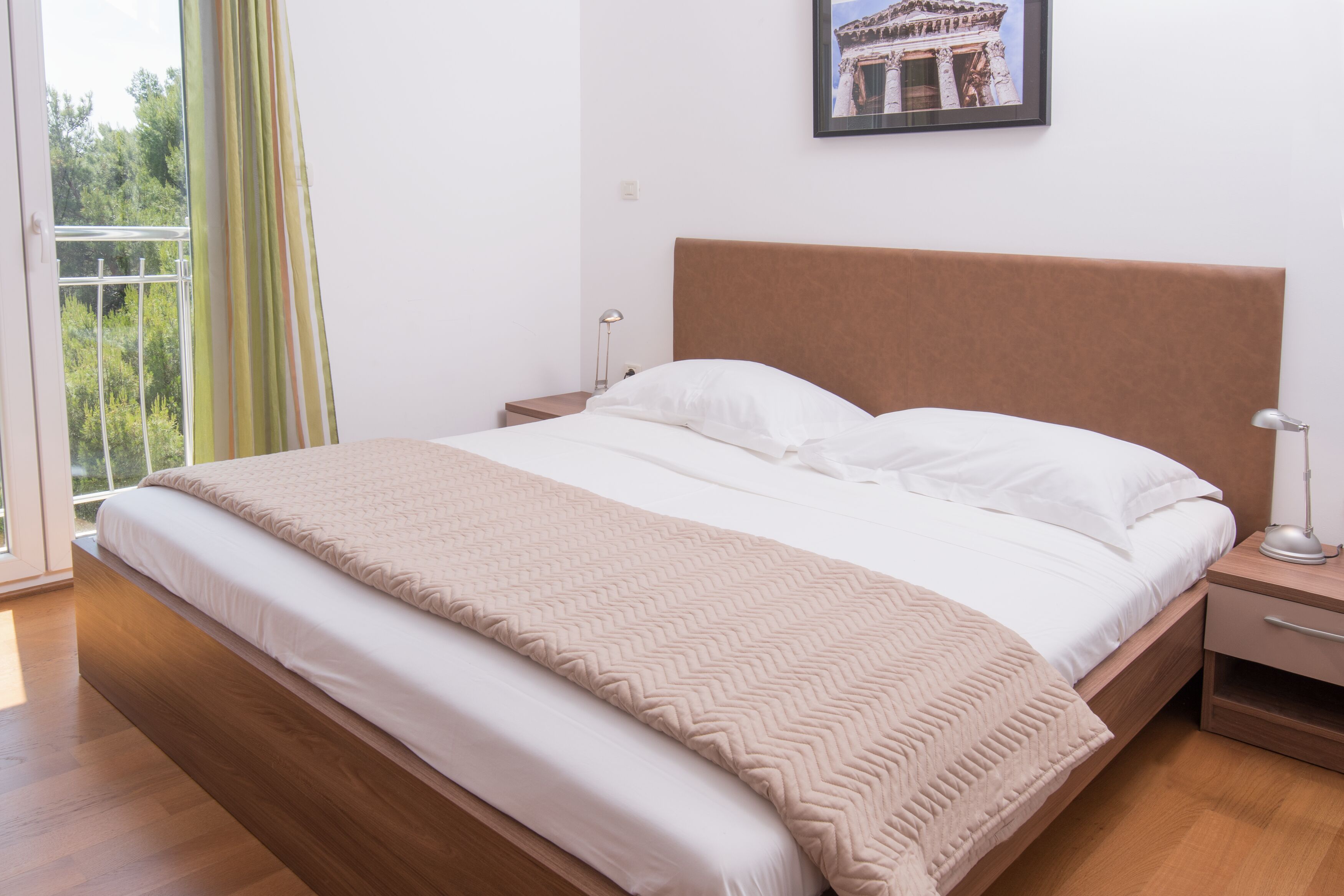 A neatly made bed with a wooden headboard, a bedside table with a lamp, and a window with curtains.