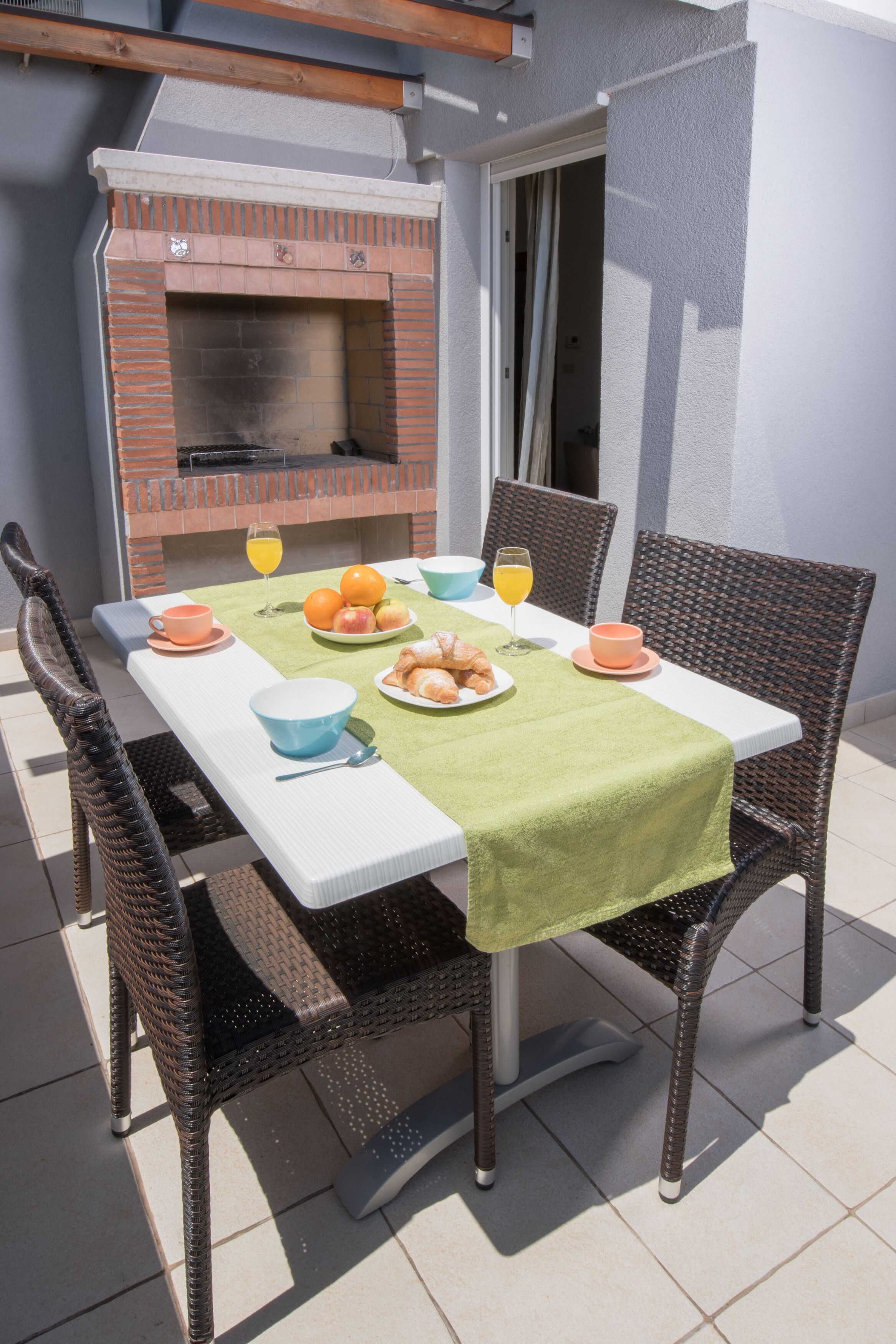 Ein Essbereich im Freien mit einem Backstein-Grill, Korbstühlen und einem Tisch, gedeckt mit Speisen und Getränken.