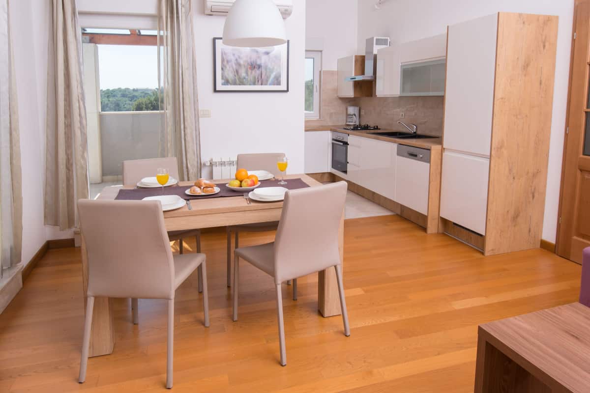 Eine moderne Küche mit Holzausstattung, einem Esstisch mit Stühlen und Blick ins Freie durch große Fenster.
