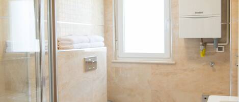 A modern bathroom with a glass shower enclosure, a bidet, a toilet, and a window providing natural light.