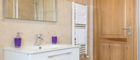 A modern bathroom with a white vanity, a large mirror, a wooden door, and a white bathtub.