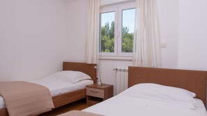 Un dormitorio con dos camas individuales, una mesita de noche, una lámpara y una ventana con cortinas.