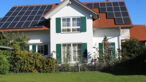 A two-story house with solar panels on the roof, green shutters, and a well-maintained lawn. - Apartment 2 in the beautiful Gutenberg / Ostallgäu (Gutenberg)