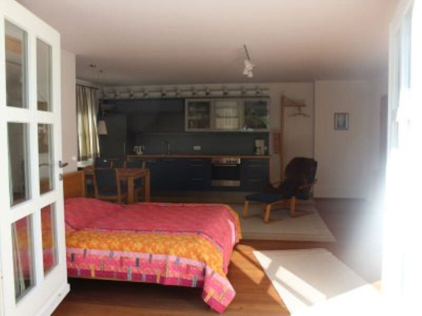 Un dormitorio con cama, escritorio y silla. Se observa una kitchenette al fondo.