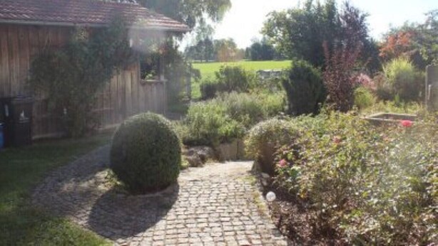 A garden with a paved path, a wooden fence, and various plants. - Apartment 2 in the beautiful Gutenberg / Ostallgäu (Gutenberg)