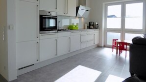 A modern kitchen with white cabinets, a built-in oven, and a large window providing natural light.