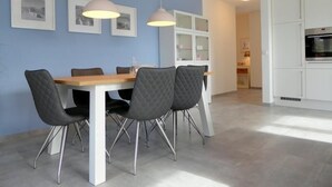 A modern kitchen with white cabinets, a dining table with four chairs, pendant lights, and framed pictures on the wall.