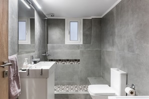 Ein modernes Badezimmer mit Dusche, Toilette und Waschbecken, mit grauen Fliesen und einer Holztür.
