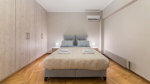 A modern bedroom with a large bed, wooden wardrobe, bedside lamps, and a built-in air conditioning unit. - Acropolis Promenade Apartment (Athens)