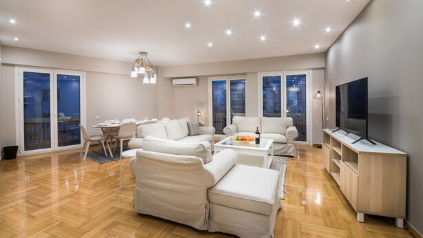 A spacious living room with a sofa set, a dining table, and a TV on a wooden cabinet. - Acropolis Promenade Apartment (Athens)