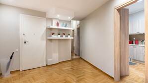 A hallway with wooden flooring, white walls, and a kitchen area visible through an open door. - Acropolis Promenade Apartment (Athens)