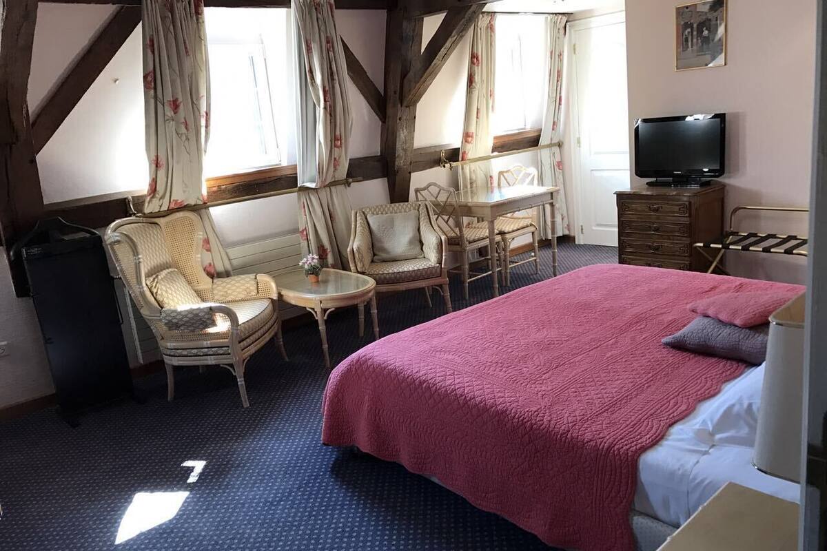 Un dormitorio con una cama grande, dos sillas, una mesita, un televisor y un aparador.