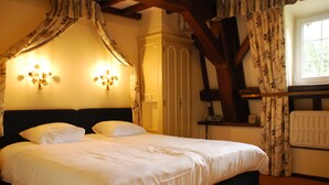 A bedroom with a canopy bed, a bedside table, and a radiator. - Hostellerie le Prieuré de Conques (Florenville)