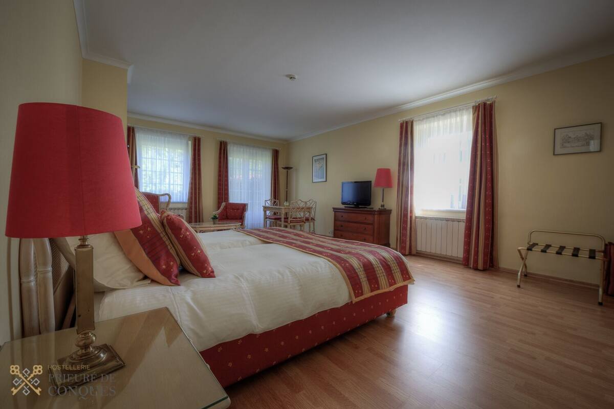 Habitación de hotel con una cama grande, un escritorio, una silla, un televisor y una ventana con cortinas.