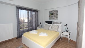 A neatly made bed with a yellow bedspread, a small bedside table with a lamp, and a wall art piece above the bed. - Edem Beach Apartment with Mountain view by Athenian Homes (Paleo Faliro)