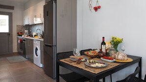 A modern kitchen with a dining area, including a refrigerator, washing machine, and a table set with food and drinks. - Edem Beach Apartment with Mountain view by Athenian Homes (Paleo Faliro)