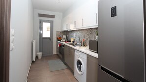 A modern kitchen with stainless steel appliances, a built-in washing machine, and a grey tiled backsplash. - Edem Beach Apartment with Mountain view by Athenian Homes (Paleo Faliro)
