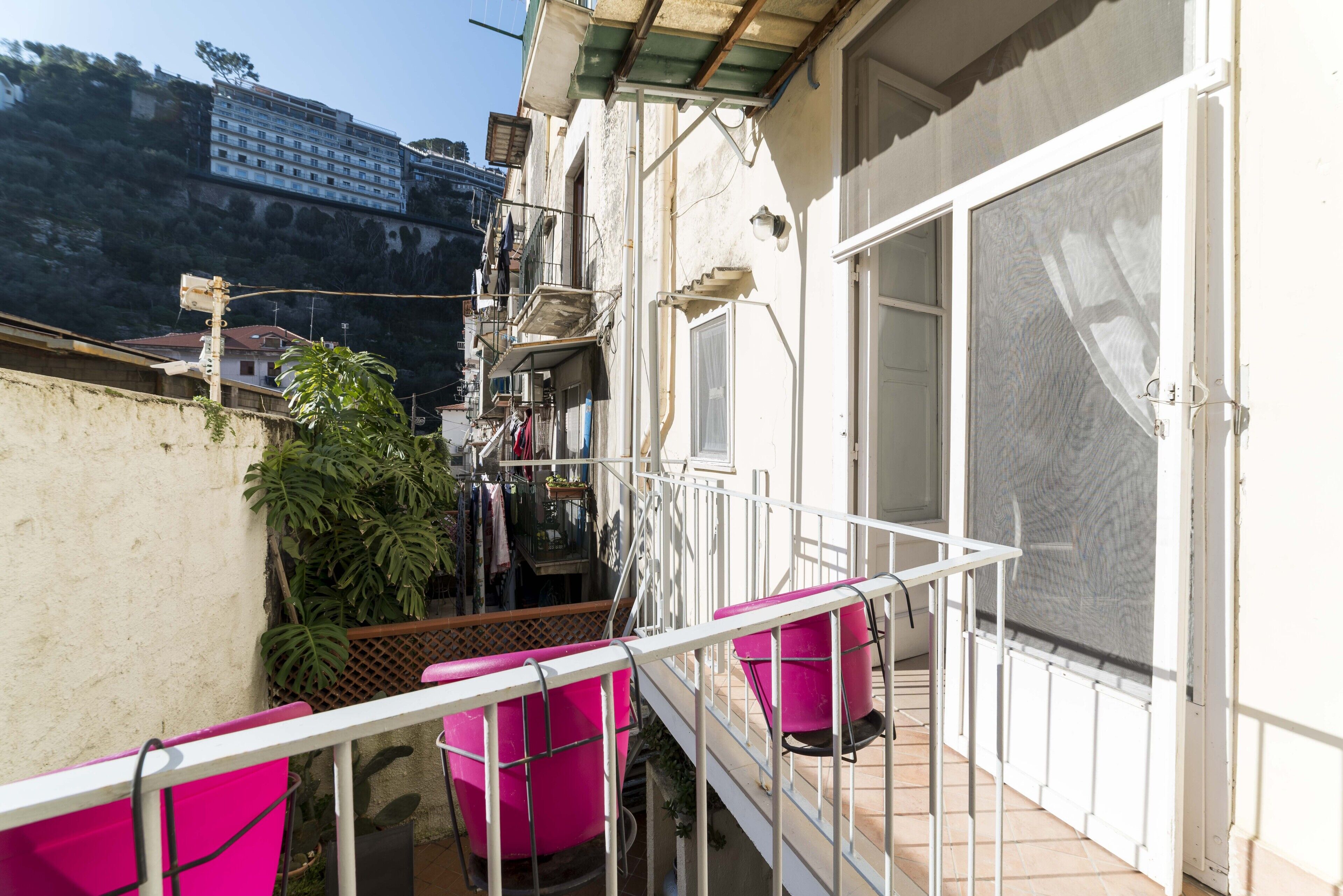 A balcony with a metal railing, a large window with a screen, and a view of a building in the background.