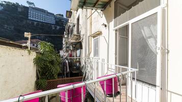 A balcony with a metal railing, a large window with a screen, and a view of a building in the background.