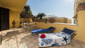 A sunlit patio with a table, chairs, and two lounge chairs. - Namily House (Positano)