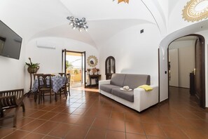 Sala de estar com sofá, mesa de jantar com cadeiras, TV fixada na parede e ventilador de teto.