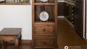 A wooden cabinet with decorative plates, a hanging metal bell, and a painting above it. - Namily House (Positano)