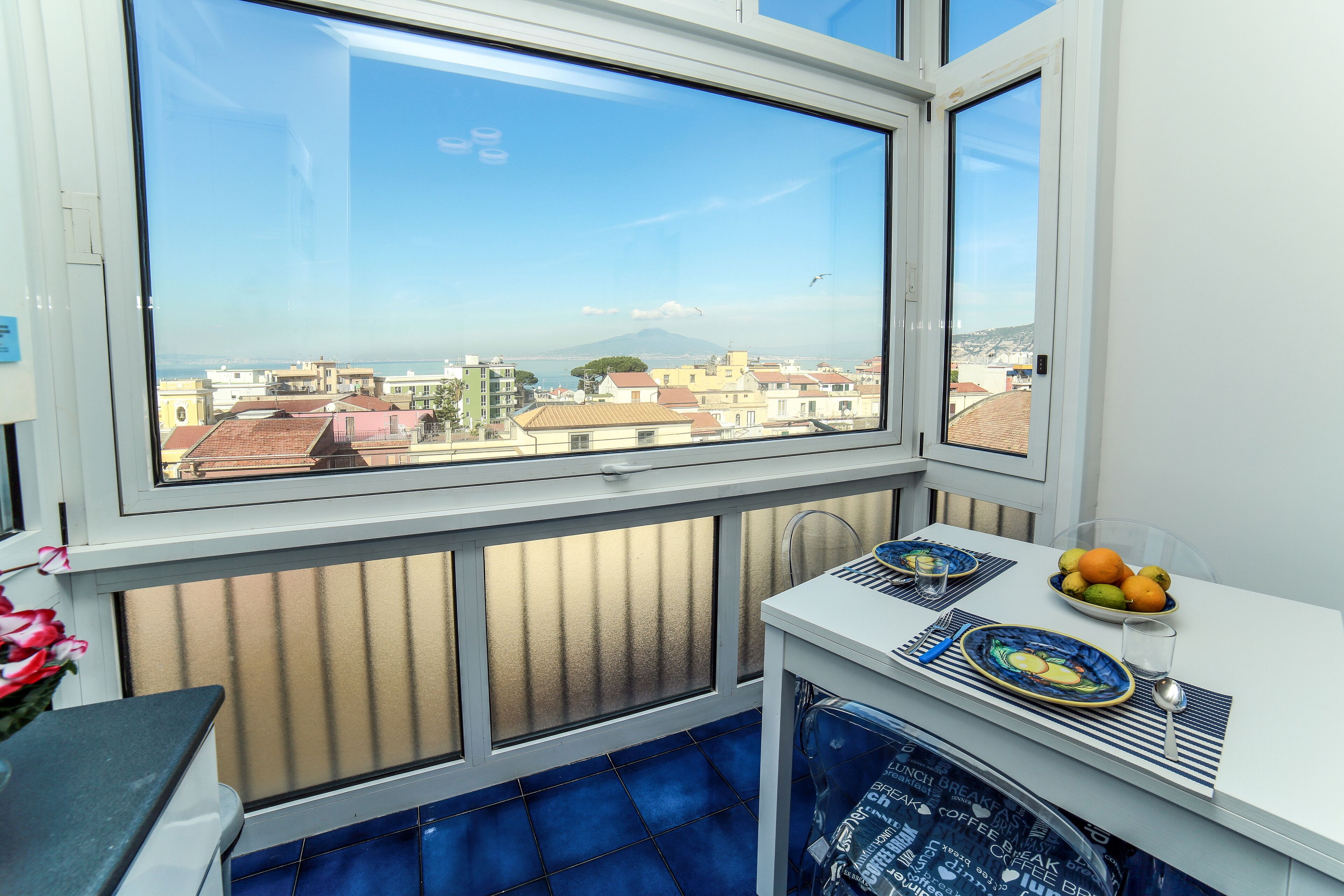 Un balcone con vista sulla città, un tavolo con un cesto di frutta e una macchina per il caffè.