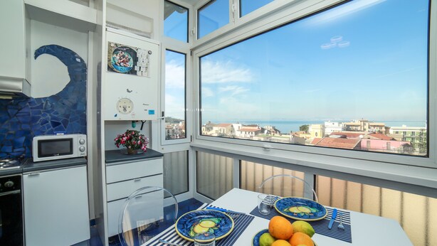 Un balcón con una mesa de comedor dispuesta con platos, cuencos y cubiertos, con vista a una ciudad costera.