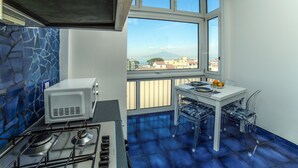 Una cocina con estufa a gas, microondas y ventana con vistas a edificios y una montaña.