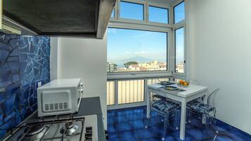 A kitchen with a gas stove, a microwave, and a window with a view of buildings and a mountain.