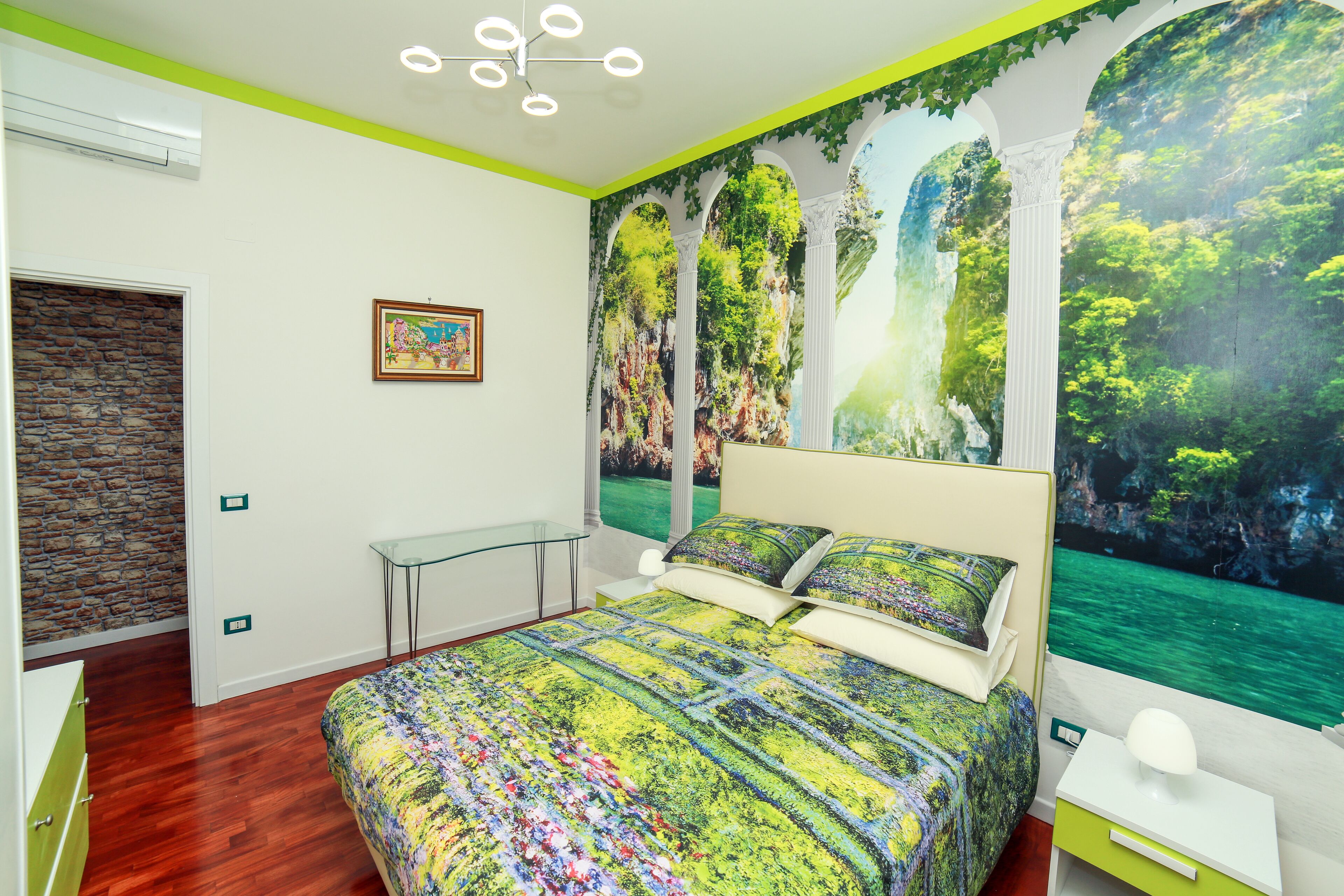 A bedroom with a bed, a glass table, a nightstand, and a mural of a forest scene.