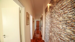 Un pasillo con suelo de madera, paredes blancas y una pared de piedra en un lateral.