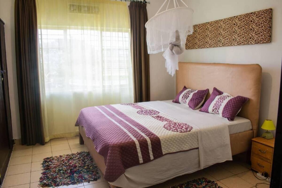 A bedroom with a bed, curtains, a bedside table, and a wall-mounted artwork.