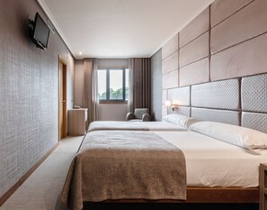 A hotel room with two beds, a television mounted on the wall, a window with curtains, and a bedside table with a lamp. - Hotel Pensua Punta del Este (Carballo)