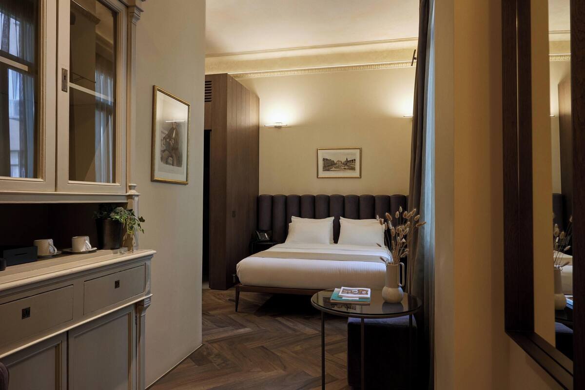 A hotel room with a bed, bedside table, and a large mirror.