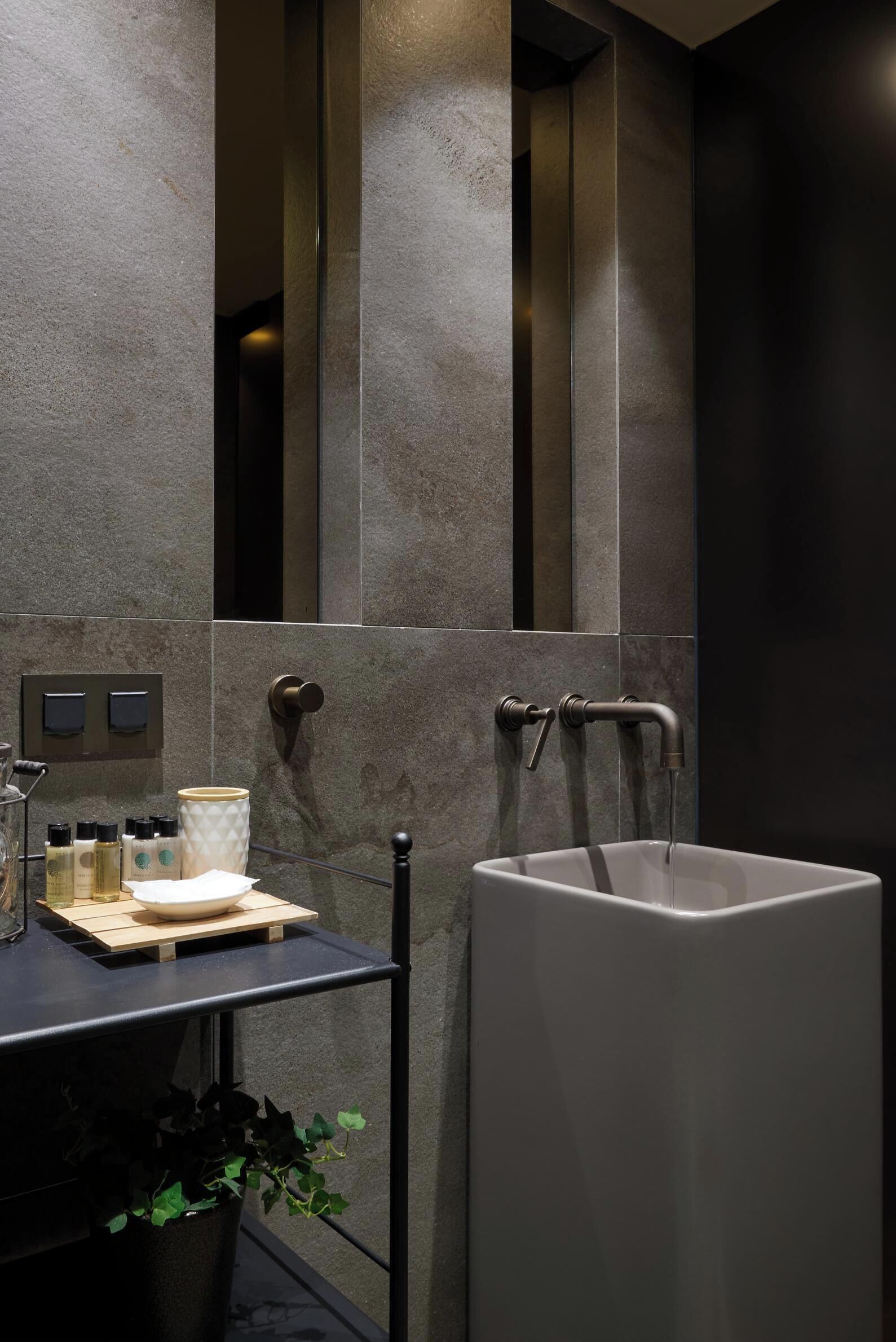 A modern bathroom with a large mirror, a white sink, and a small shelf with toiletries.