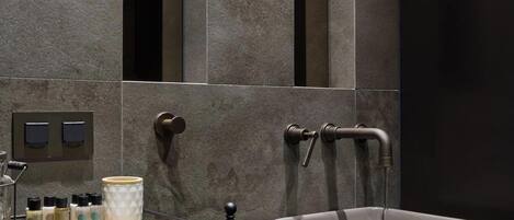 A modern bathroom with a large mirror, a white sink, and a small shelf with toiletries.