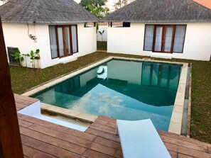 pool area surrounded by a wooden deck and two buildings with windows and white curtains.