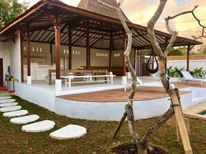 Relax in a serene outdoor space with a wooden structure, seating area, and a unique tree in the foreground.