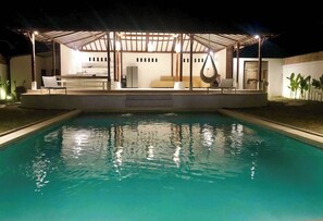 Relax by the pool under a covered pergola, surrounded by lounge chairs and a hammock.