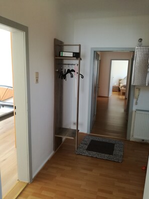 A hallway with a coat rack, a small shelf with a box, and a door leading to another room.