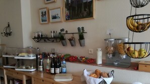 A kitchen counter with various food items, a bread basket, and hanging baskets with bananas and apples. - Gästezimmer  Weingut Peter (Wachenheim an der Weinstrasse)