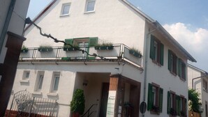 A white building with green shutters, a balcony with potted plants, and a sign reading "Weingut Peter Weinberg." - Gästezimmer  Weingut Peter (Wachenheim an der Weinstrasse)