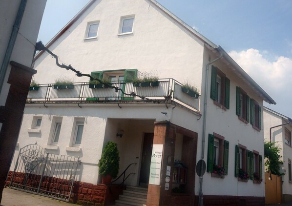 A white building with green shutters, a balcony with potted plants, and a sign reading "Weingut Peter Weinberg."