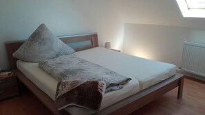 A bedroom with a wooden bed, a bedside table, a nightstand, a lamp, and a radiator. - Gästezimmer  Weingut Peter (Wachenheim an der Weinstrasse)