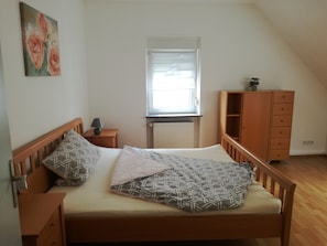 A bedroom with a bed, a nightstand, a dresser, a window with blinds, and a radiator.