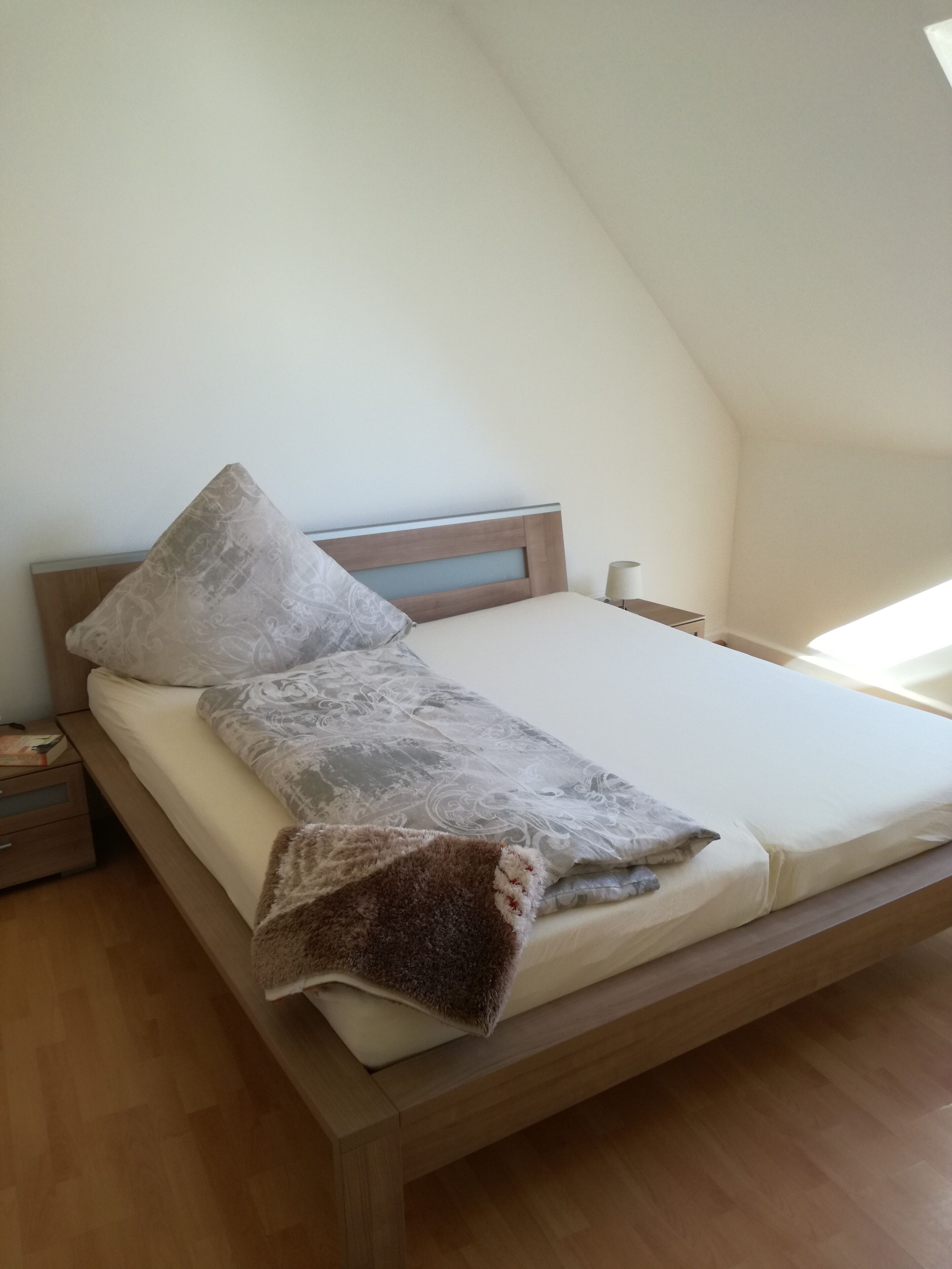 A single bed with a wooden headboard, a grey patterned pillow, and a brown blanket.