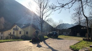Un camino adoquinado que conduce a una casa amarilla con balcón, rodeada de árboles sin hojas y una montaña al fondo.