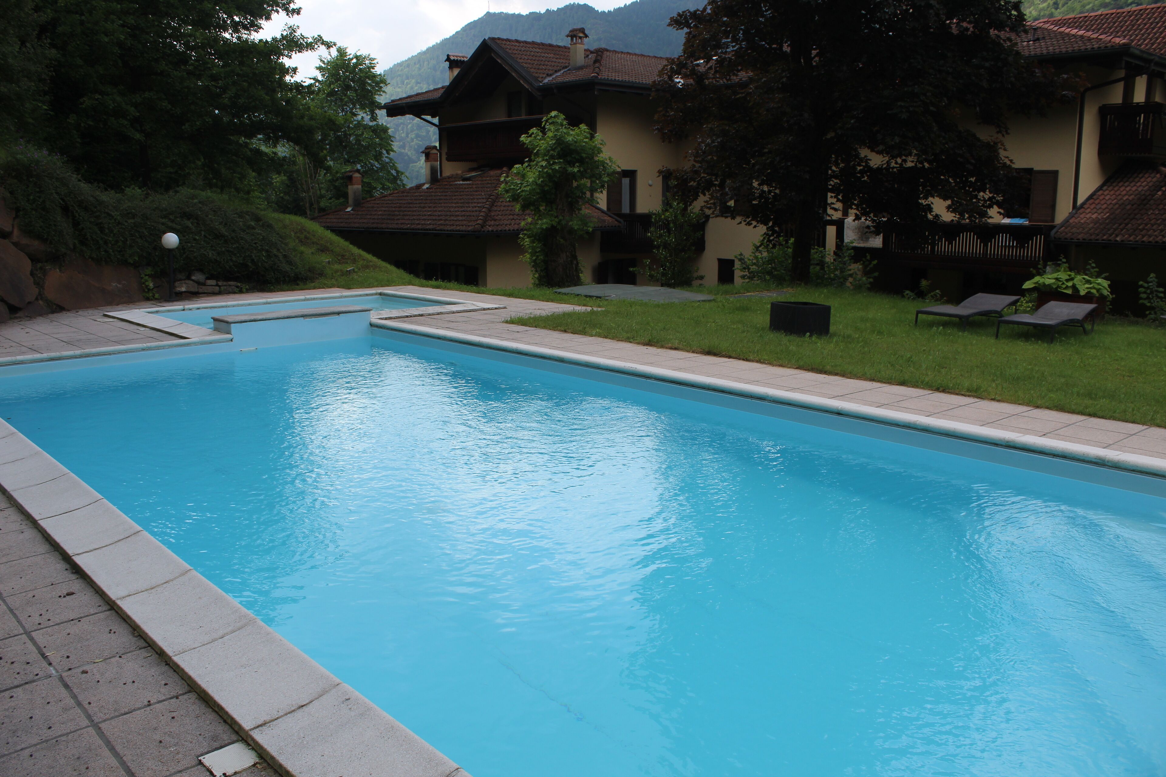 Une piscine offrant une vue dégagée sur les environs, notamment sur un bâtiment doté d’un balcon et sur une pelouse verdoyante.