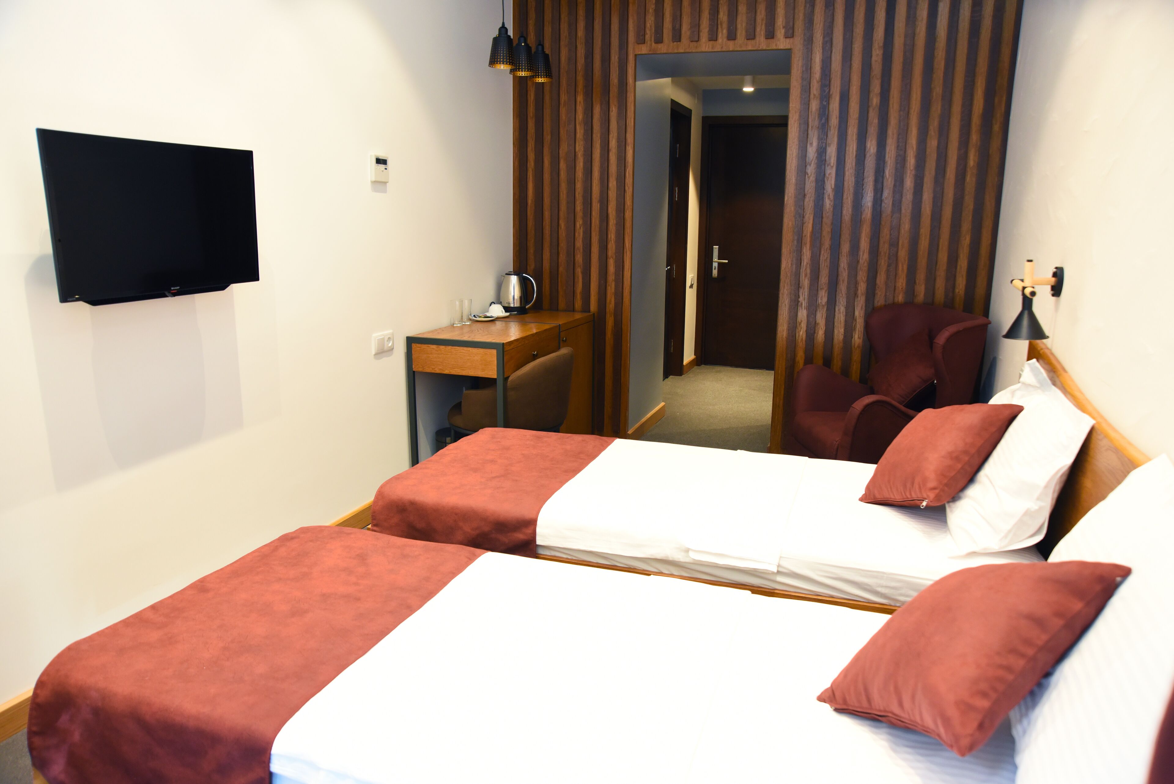Camera d'albergo con due letti, una scrivania, una sedia, una televisione e una porta che conduce a un'altra stanza.